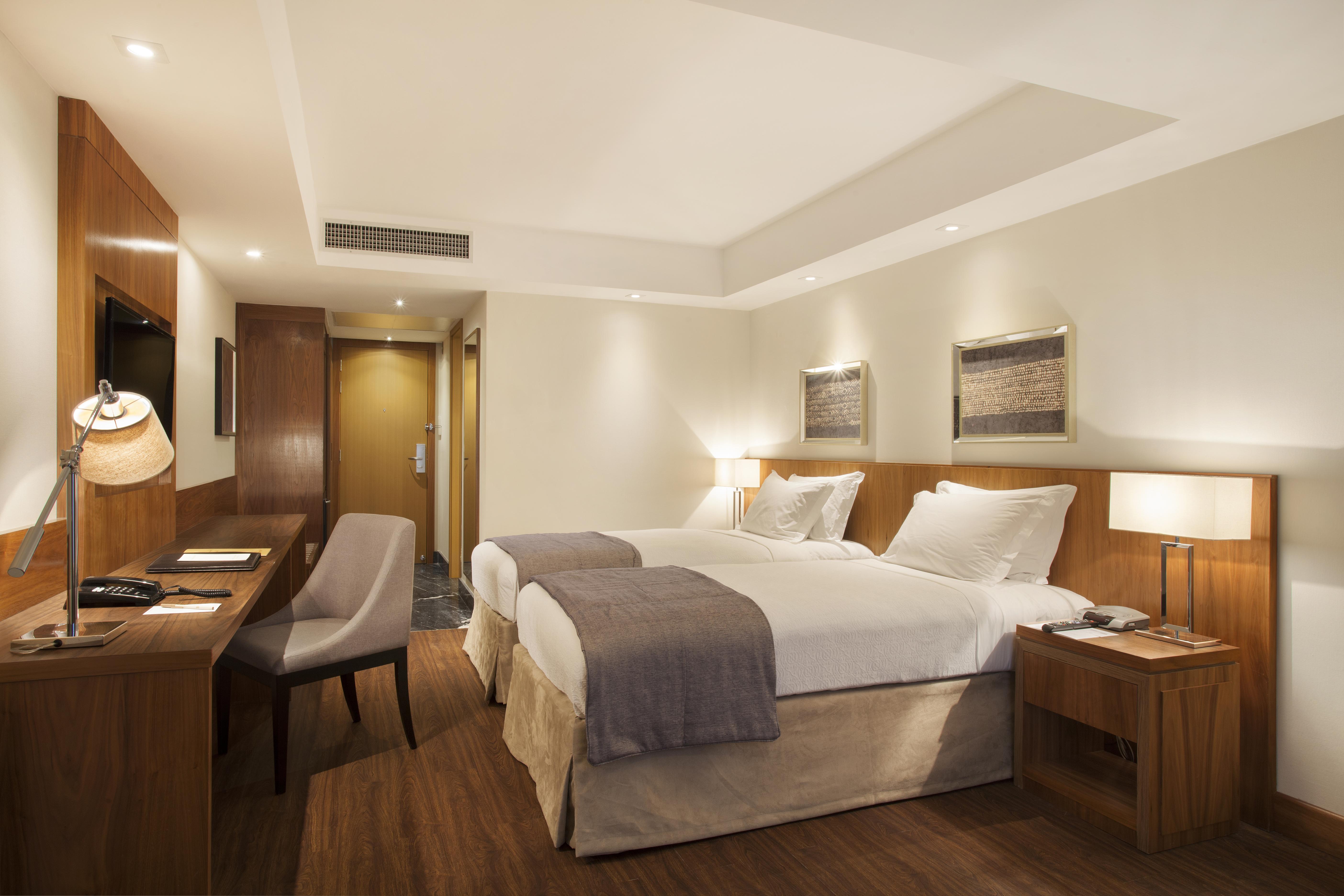 Windsor Marapendi Hotel Ρίο ντε Τζανέιρο Εξωτερικό φωτογραφία The photo displays a modern hotel room featuring two twin beds with crisp white linens and gray throw blankets. The room has a clean and minimalist design, with wooden accents, including a bedside table and a desk. To the left, there's a small desk a